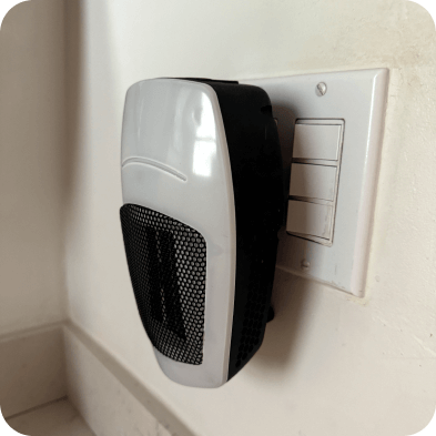 A compact heater plugged into a wall outlet beside a switch plate.
